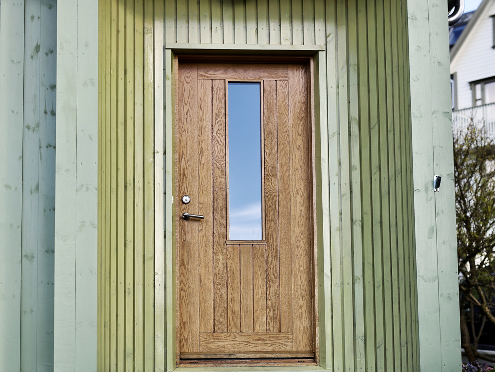 Ny inngangsdør tegnet av arkitekten. Inngangspartiet har også fått en liten ny signatur i sideveggene som er avrundet og kledd med stående smale bord. Foto: Lise Bjelland