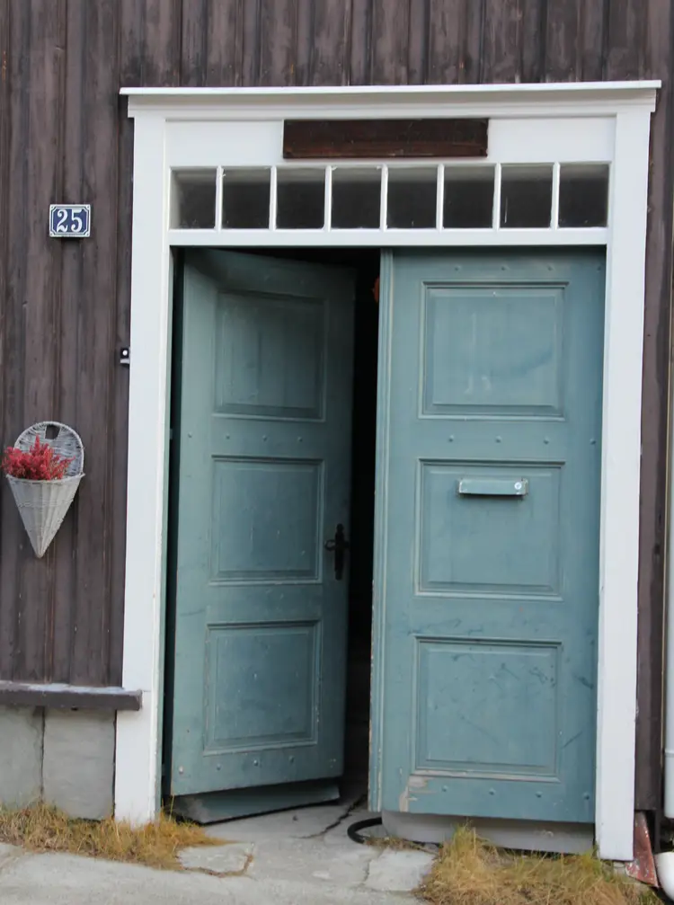 Lys koboltblå dør med hvit omramming mot brunmalt vegg. Røros. Foto: Christel Wigen Grøndahl, Bygg og Bevar