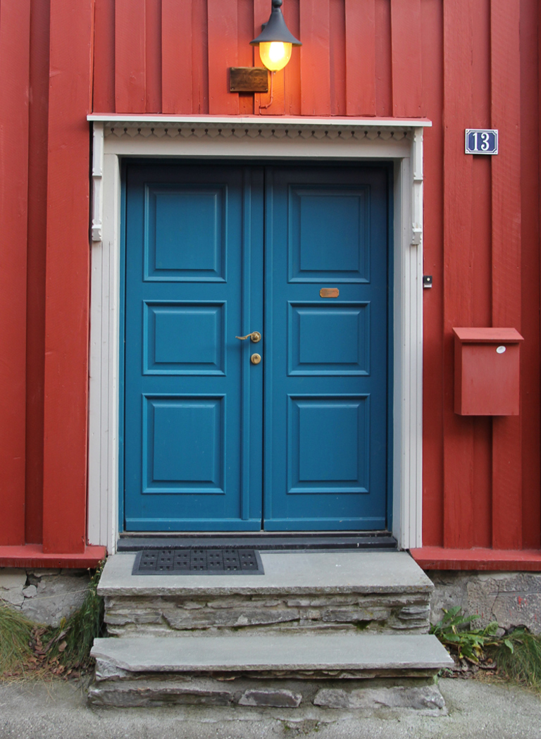 Blå dør, med hvit omramming mot rød husvegg. Røros. Foto: Christel Wigen Grøndahl, Bygg og Bevar