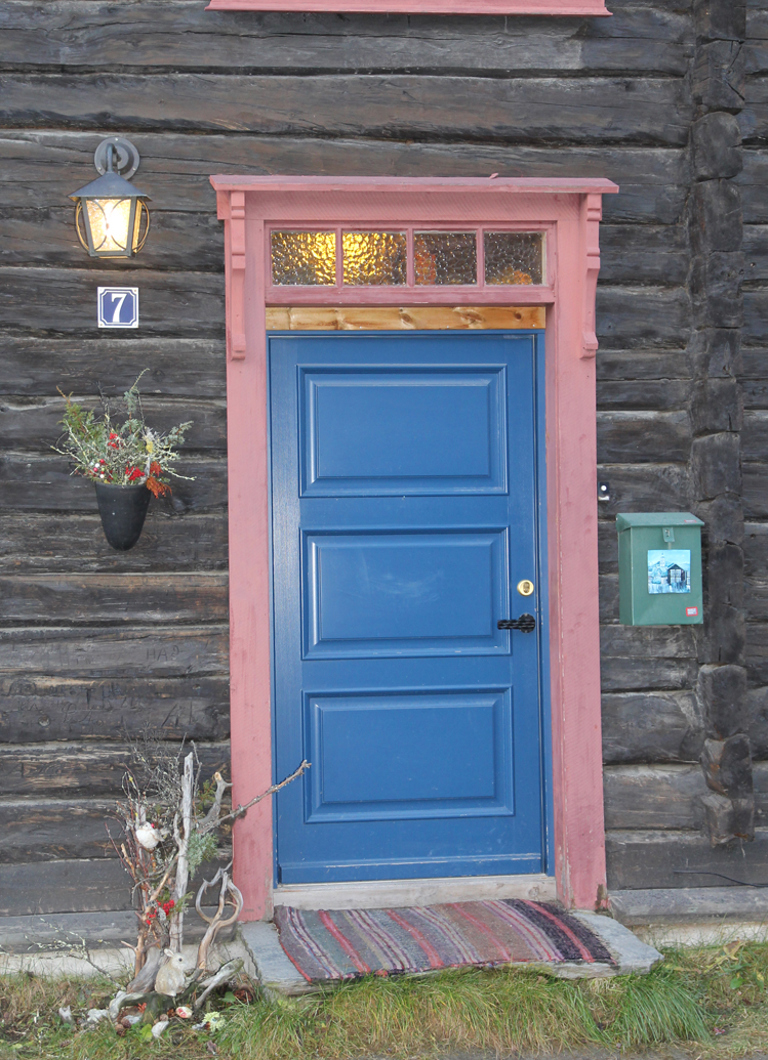Blå dør med rød omramming mot umalt tømmervegg. Røros. Foto: Christel Wigen Grøndahl, Bygg og Bevar